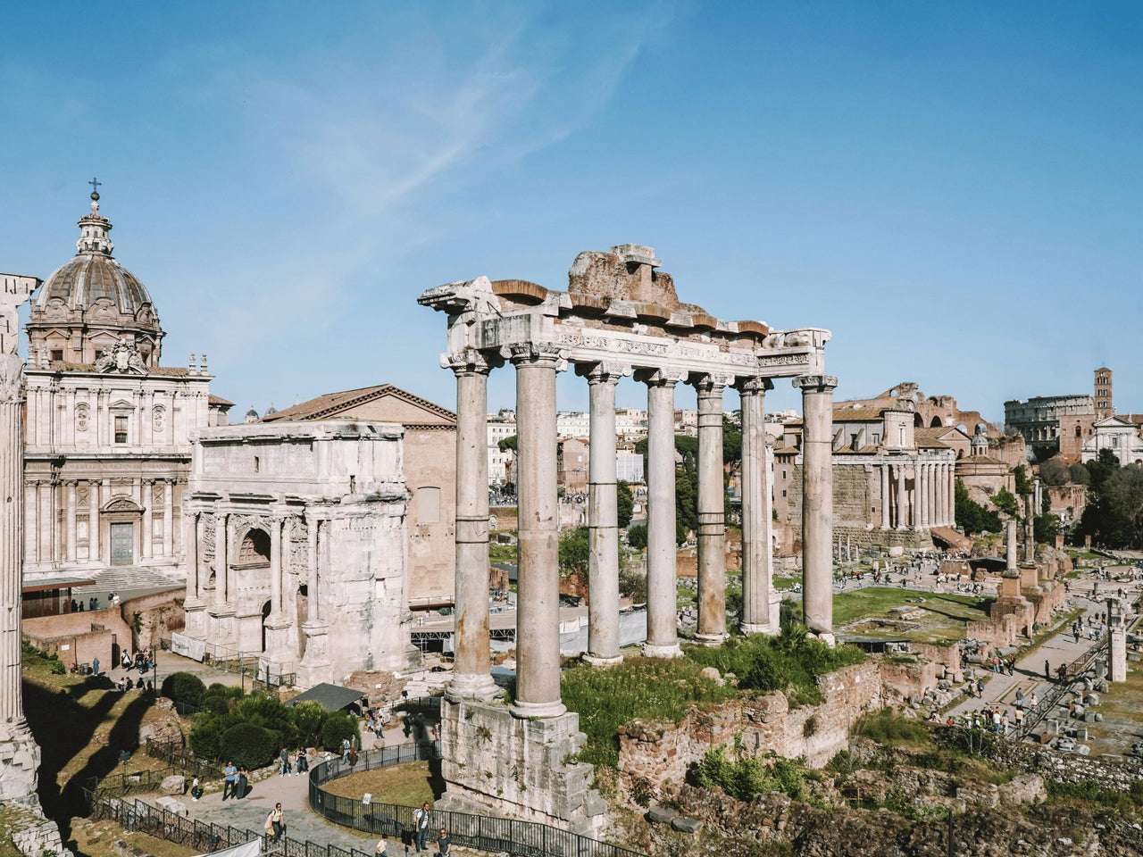 The ruins of the Roman Forum in Rome, Italy, featuring ancient temple columns and historic structures under a bright blue sky.