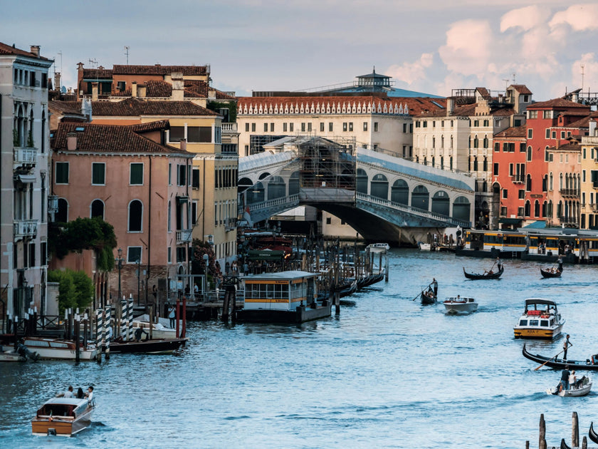 View of the Grand Canal in Venice, Italy, with gondolas and boats on the water and the iconic Rialto Bridge in the background.