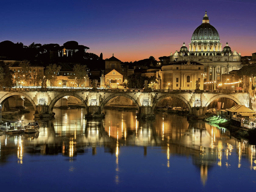 Night view of the Vatican City and St. Peter's Basilica in Rome, Italy, with the illuminated Sant'Angelo Bridge reflecting in the Tiber River.